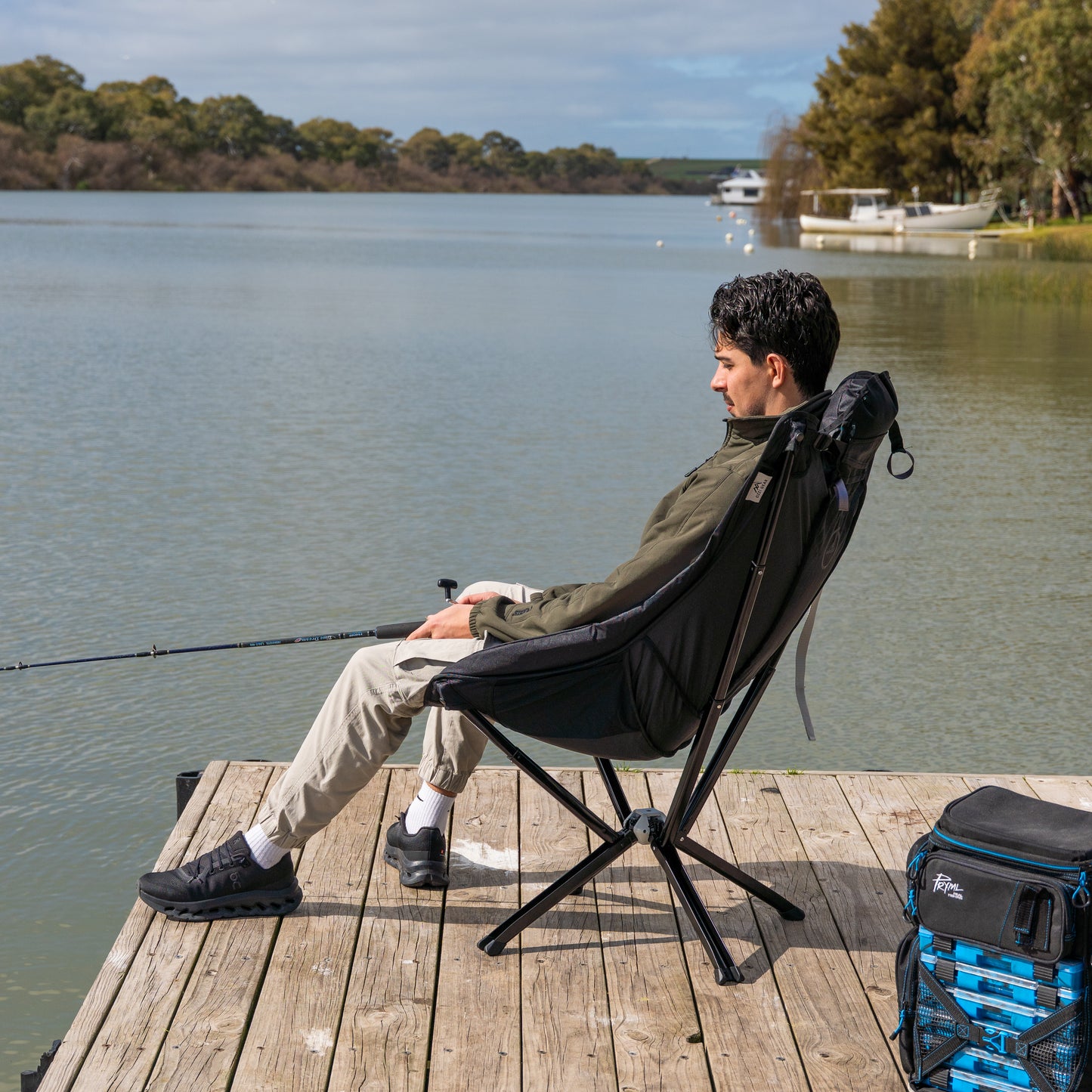 Man sitting on a black Ozzi Gear lounger fishing by the lake