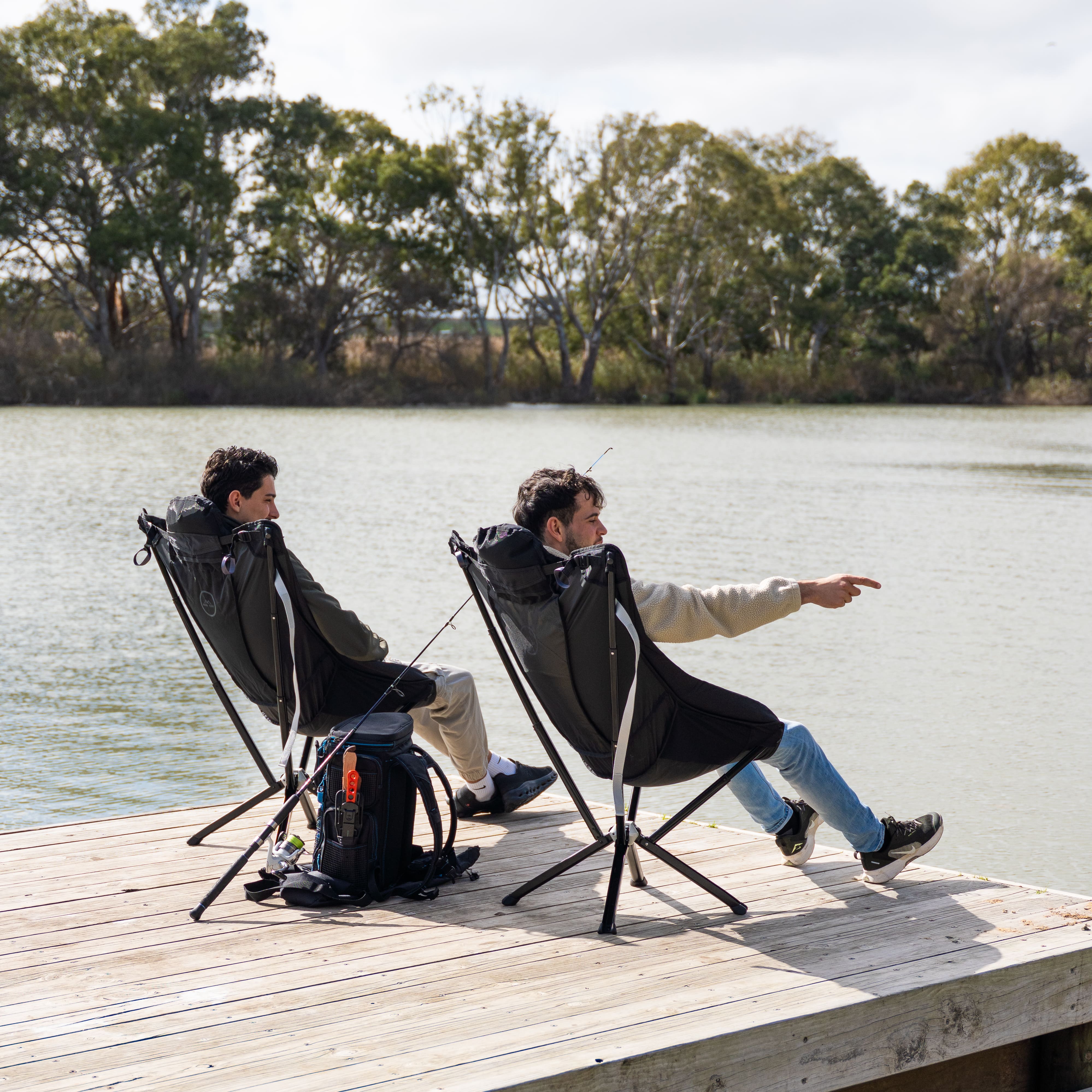 Two people sitting on camping chairs by a lake, enjoying a fishing trip.